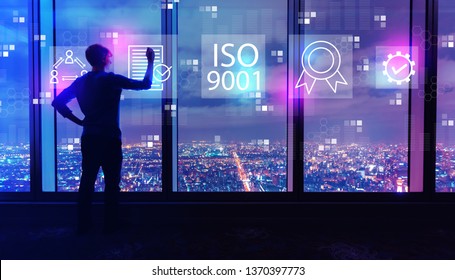 ISO 9001 With Man Writing On Large Windows High Above A Sprawling City At Night