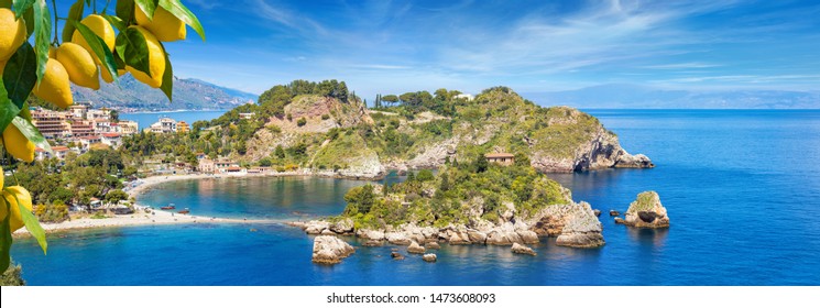 Isola Bella is small island near Taormina, Sicily, Italy. Narrow path connects island to mainland Taormina beach in azure waters of Ionian Sea. Bunches of fresh yellow ripe lemons on foreground.