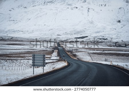 Isolate car driving across Ring Road asphalt highway in Iceland, cutting through a white, snowy gigantic mountain landscape in winter,  remote travel in the countryside highlands Eastfjords