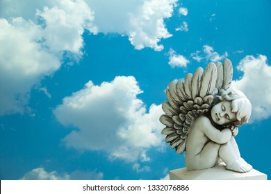 Isolate of cupid,  little angel and blue sky.The angel statue is sitting asleep on a blue sky.