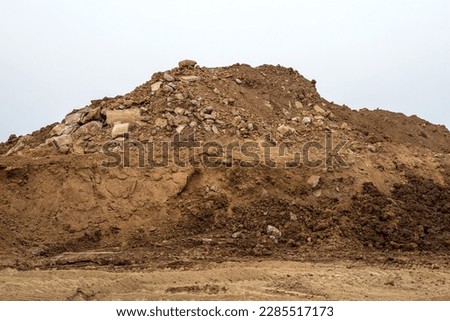 Isolate mounds of sand and concrete debris that have been excavated and poured together to prepare materials for filling and repairing roads in rural Thailand during the dry season.