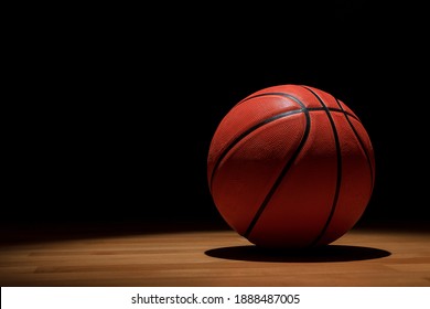 ISOLATED BASKETBALL ON WOODEN COURT WITH SPOTLIGHTS FROM ABOVE AND DARK BACKGROUND WHEN THE GAME IS OVER. TRAINING, MATCH AND CHAMPIONSHIP IN COLLEGE AND UNIVERSITY CAMPUS. COPY SPACE.