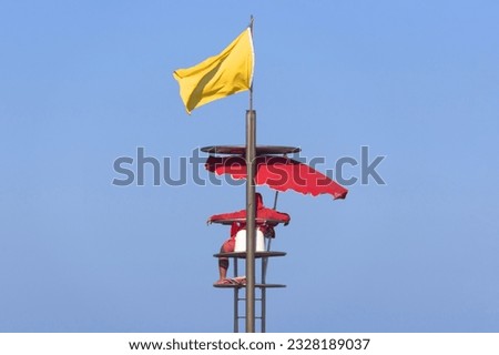 An isolated beach lifeguard station against a blue backdrop, displays a yellow flag, symbolizing caution and warning for swimmers