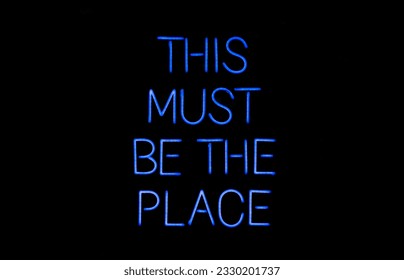 Isolated blue neon sign on black background that says 'this must be the place' 