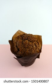 Isolated Bran Muffin Wrapped In Paper Against A Pink And Blue Background