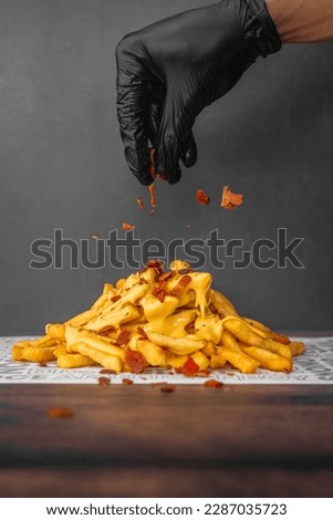 Isolated close up photo of a hand pulling bacon into French fries loaded with cheese in a dark background