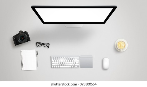 Isolated computer display for mockup on work desk with keyboard, mouse, coffee, camera, notebook, glasses, pencil.