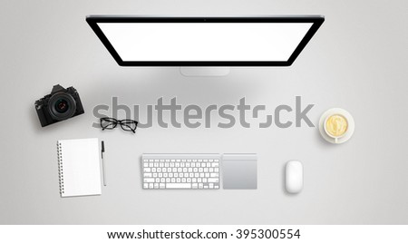 Isolated computer display for mockup on work desk with keyboard, mouse, coffee, camera, notebook, glasses, pencil.