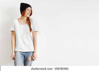Isolated cropped portrait of fashionable stylish young woman model wearing trendy clothes looking away, laughing cheerfully while having fun indoors, posing at studio wall in trendy clothing