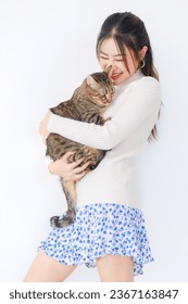 Isolated cutout studio shot Asian young pretty  female teenager girl model in turtleneck sweater standing holding cute little domestic tabby short hair companion pet cat kitty on white background. - Shutterstock ID 2367163847