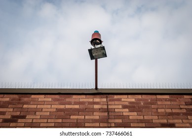 Isolated External Lamp. Halogen Lamp On Exterior Of Building Facade. Rooftop With Hanging Flood Light. Pigeon Spikes On Roof. Architectural Detail. Abstract Colors.