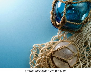 Isolated Glass Buoys On Fishing Net With Blue Tinge As If Washed In By A Wave Against Bright Light Blue Background