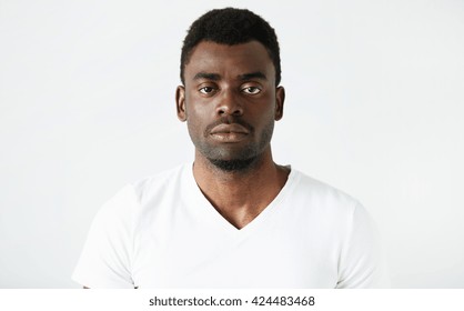 Isolated Headshot Of Handsome African American Adult Man In White T-shirt, Looking At The Camera With Serious And Confident Expression On His Face Posing Against White Studio Wall Background.