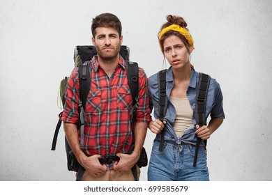 Isolated Horizontal Portrait Of Stylish Tired Worn Out Young Caucasian Man And Woman Travelers Or Hitchhikers Carrying Heavy Backpacks Feeling Exhausted After Difficult Trekking In Mountains