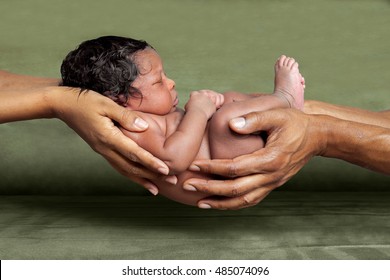 An isolated image of African American parent hands holding their newborn, baby girl in front of a green background.
