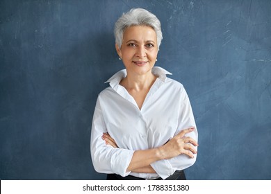 Isolated Image Of Stylish Successful 50 Year Old Female Broker In White Shirt Posing Against Blank Studio Wall Background, Crossing Arms On Her Chest, Having Confident Facial Expression, Smiling