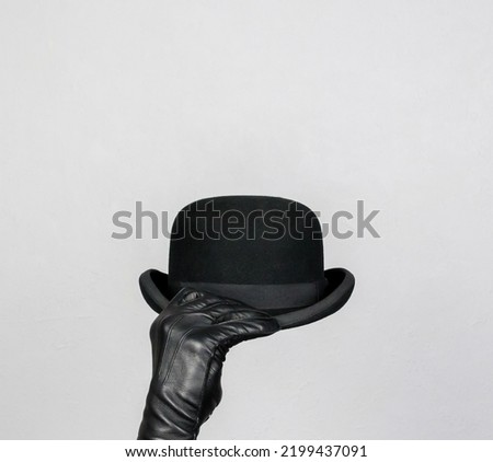 Isolated Leather Glove Hand Holding Bowler Hat on White Background. Concept of British Butler or English Gentleman.