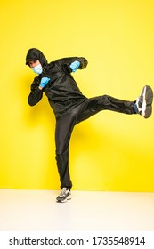 Isolated Man On Yellow Background In Full Body Black Costume, With Medical Mask And Steril Gloves  Jumping