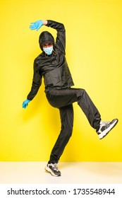 Isolated Man On Yellow Background In Full Body Black Costume, With Medical Mask And Steril Gloves In Fight Position Or Dancing Moves