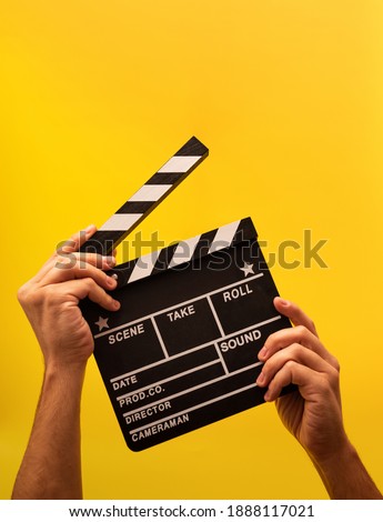 Isolated movie clapperboard gripped by male hands on yellow background