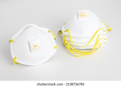 Isolated N95 Facemask With Yellow Straps Beside Stack Of Facemasks On White Background