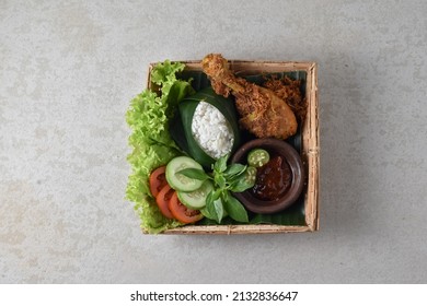 Isolated Nasi Ayam Goreng Serundeng or Rice with Crispy fried chicken of Javanese style. Served on bamboo plate with fresh vegetables and chilli shrimp paste. Usually called Ayam Goreng Lamongan.