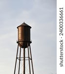 Isolated old, brown water tower against a light and cloudy sky