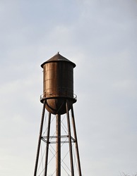 Isolated Old, Brown Water Tower Against A Light And Cloudy Sky