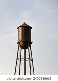 Isolated old, brown water tower against a light and cloudy sky