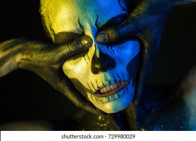 Isolated on black, closeup picture, toned yellow and blue, spooky young blonde caucasian pretty woman with scull body art, closed grey eyes, closes her eyes with her thumbs