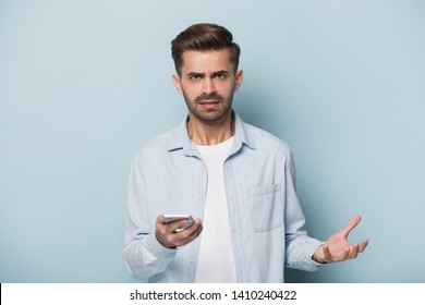 Isolated On Blue Background Angry Annoyed Man Frowns Look At Camera Holding Smart Phone Having Problems With Wi-fi No Wireless Connection, Need Repair Broken Phone, Unpleasant Message Received Concept