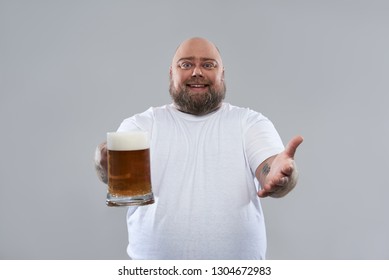 Isolated on the grey background photo of positive bearded man holding a big glass of beer and smiling
