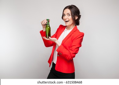 Isolated on grey, beautiful caucasian brunette woman dressed in red jacket and white shirt stand and hold glass bottle, look at camera, happy, amazed