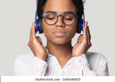 Isolated on grey studio background close up african young beautiful serene woman wearing blue headphones spend free time listen favourite music, usage of application on-line, mood and hobby concept - Powered by Shutterstock