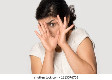 Isolated on grey studio background young indian afraid terrified woman hiding behind hands, trying to avoid something scared, making rejecting gesture, looking at camera, head shot close up portrait. - Shutterstock ID 1613076703
