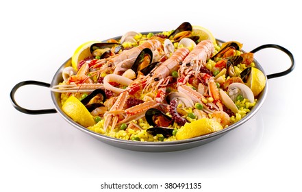 Isolated pan full of cooked large shrimp, yellow rice, clams and green peas with lemon wedges over white background