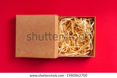 Isolated photo of carboard box packaging with sawdust on red background.