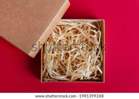 Isolated photo of carboard box packaging with sawdust on red background.