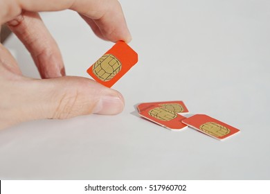 Isolated Photo Of Male Hand Holding Red SIM Card Above A Group Of 3 Other SIM Cards Used In The Mobile Phones (cell Phone Devices) With A Focus On Their Golden Micro Chip 