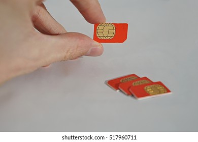 Isolated Photo Of Male Hand Holding Red SIM Card Above A Group Of 3 Other SIM Cards Used In The Mobile Phones (cell Phone Devices) With A Focus On Their Golden Micro Chip 