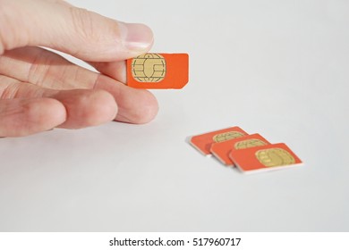 Isolated Photo Of Male Hand Holding Red SIM Card Above A Group Of 3 Other SIM Cards Used In The Mobile Phones (cell Phone Devices) With A Focus On Their Golden Micro Chip 