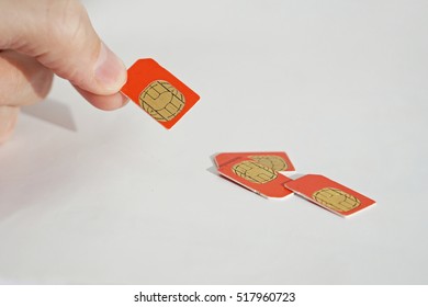 Isolated Photo Of Male Hand Holding Red SIM Card Above A Group Of 3 Other SIM Cards Used In The Mobile Phones (cell Phone Devices) With A Focus On Their Golden Micro Chip 