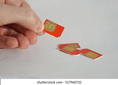 Isolated Photo Of Male Hand Holding Red SIM Card Above A Group Of 3 Other SIM Cards Used In The Mobile Phones (cell Phone Devices) With A Focus On Their Golden Micro Chip 