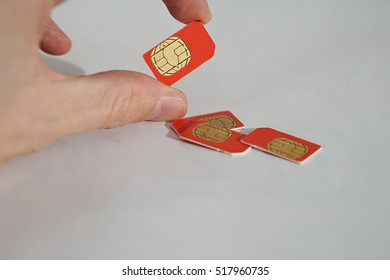 Isolated Photo Of Male Hand Holding Red SIM Card Above A Group Of 3 Other SIM Cards Used In The Mobile Phones (cell Phone Devices) With A Focus On Their Golden Micro Chip 