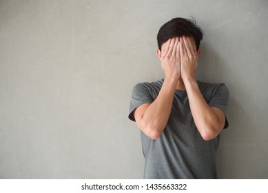 Isolated Portrait Asian Man In Casual Clothes Covers His Face By Hands With Loft Cement Wall In Background. Sad Man.