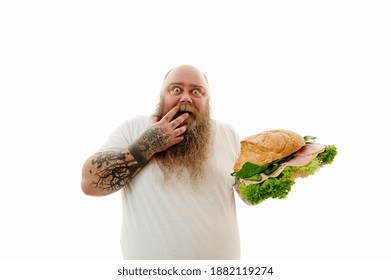 Isolated Portrait On A White Background Of A Fat Man Covering Hid Mouth With One Hand Holding And A Huge Burger On The Other Hand