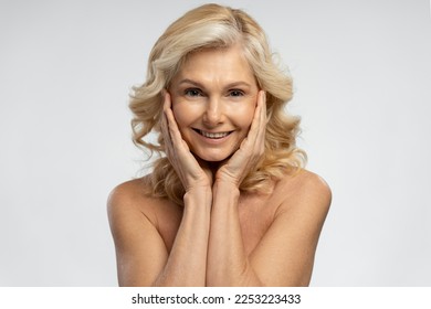 Isolated portrait on white background of charming attractive 50 years mature woman with blond shiny hair, holding hands on her face and smiling toothy smile looking at camera. Beauty treatment concept