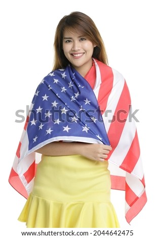 Isolated portrait shot of beautiful young Asian girl stand holding showing large United States of America national flag in front white background represent celebration on 4th of July independence day.