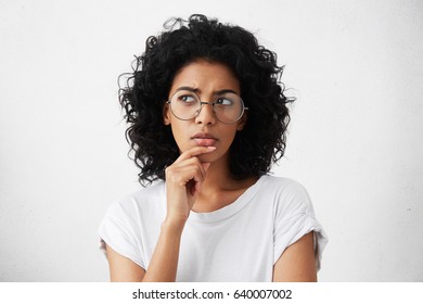 Isolated portrait of stylish young mixed race woman with dark shaggy hair touching her chin and looking sideways with doubtful and sceptical expression, suspecting her boyfriend of lying to her - Shutterstock ID 640007002