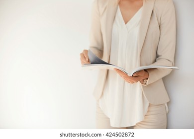 Isolated portrait of young stylish woman wearing formal suit, reading fashion magazine and looking for information on trends, during short break in the office. Lifestyle concept. Selective focus - Powered by Shutterstock